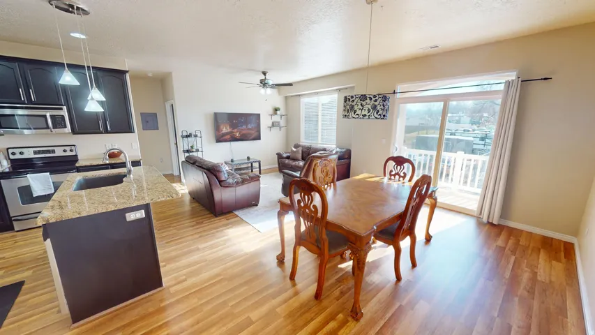 Open-concept living area featuring wood-finish flooring, a kitchen island with granite countertop, dark wood cabinetry, stainless steel appliances, and a sliding glass door leading to an outdoor deck