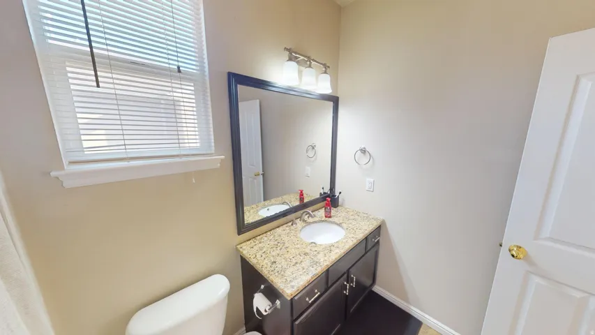 Vanity with a speckled stone countertop, undermount sink, and dark wood-finish cabinetry