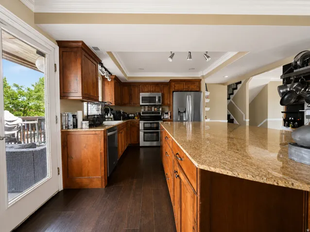 Kitchen featuring a spacious island with a polished stone countertop, rich wood cabinetry, stainless steel appliances, and dark wood-finish flooring