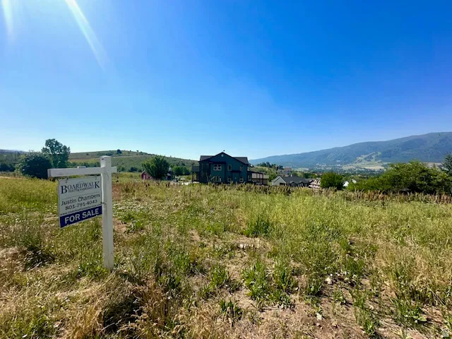 Expansive land parcel featuring natural ground cover, distant mountain ranges, and nearby residential structures