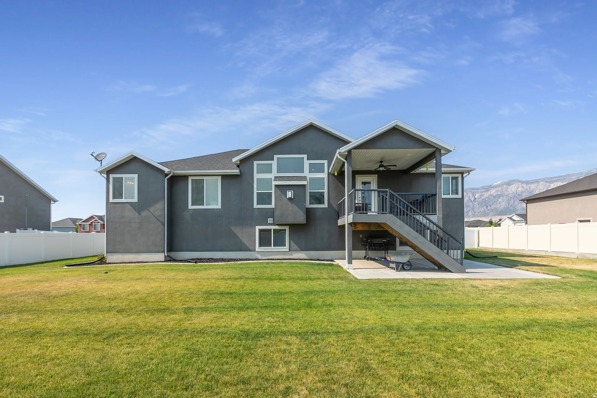 Rear exterior featuring a large covered deck with ceiling fan, a ground-level concrete patio, and a spacious grassy yard