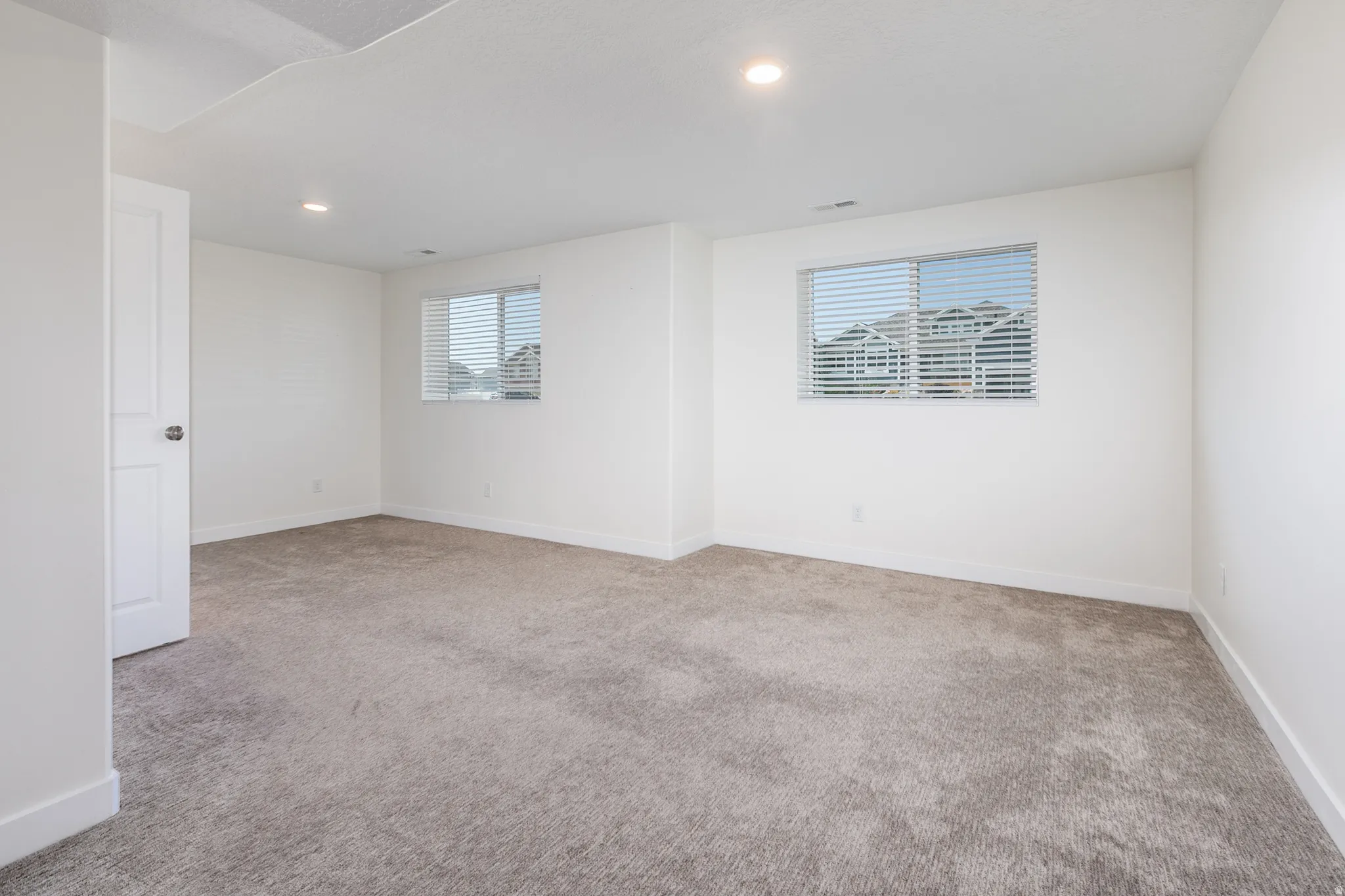 Spacious room featuring neutral carpeting, recessed lighting, and two windows with blinds