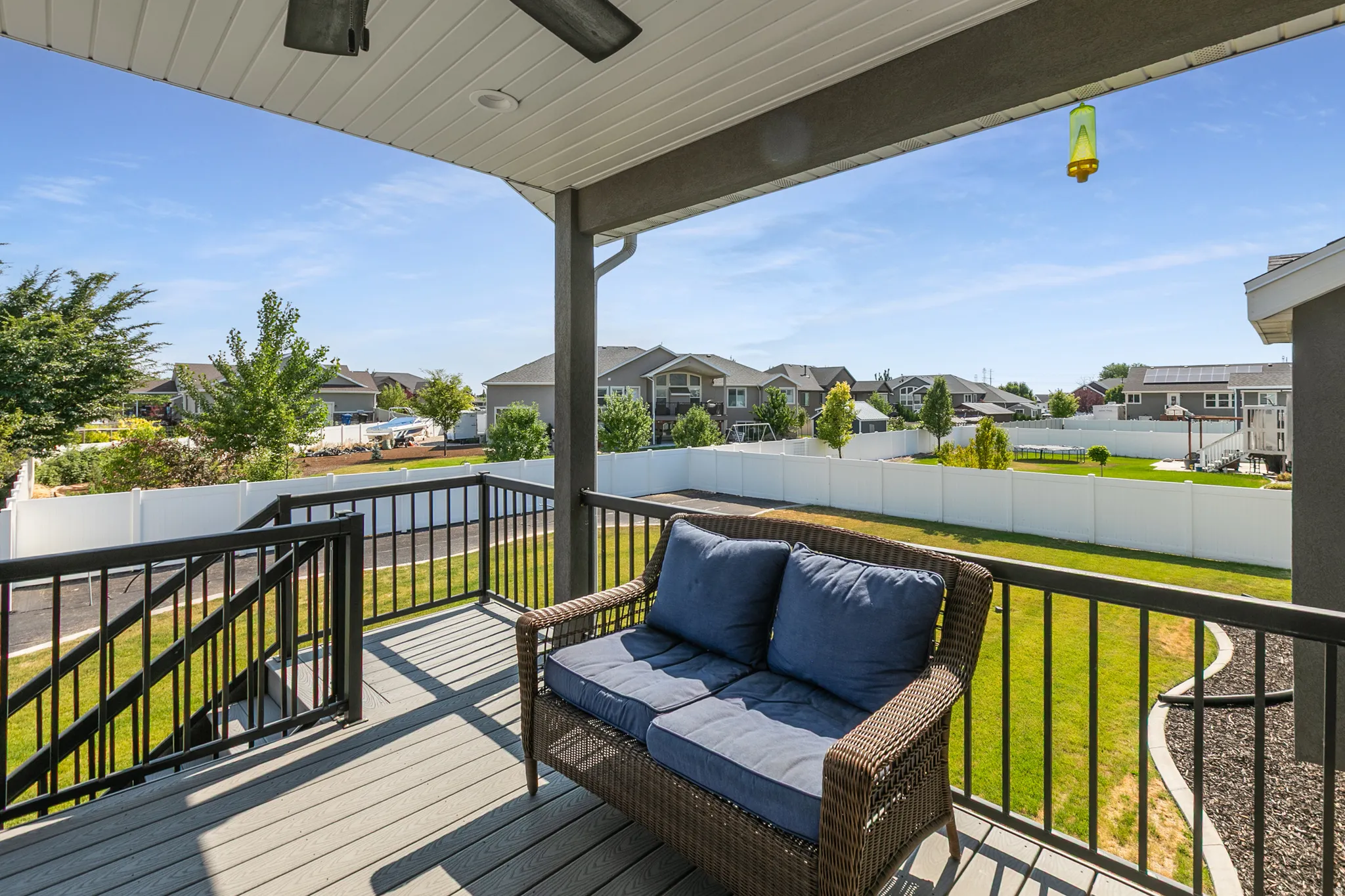 Covered deck featuring composite decking, black metal railings, and a white vinyl privacy fence