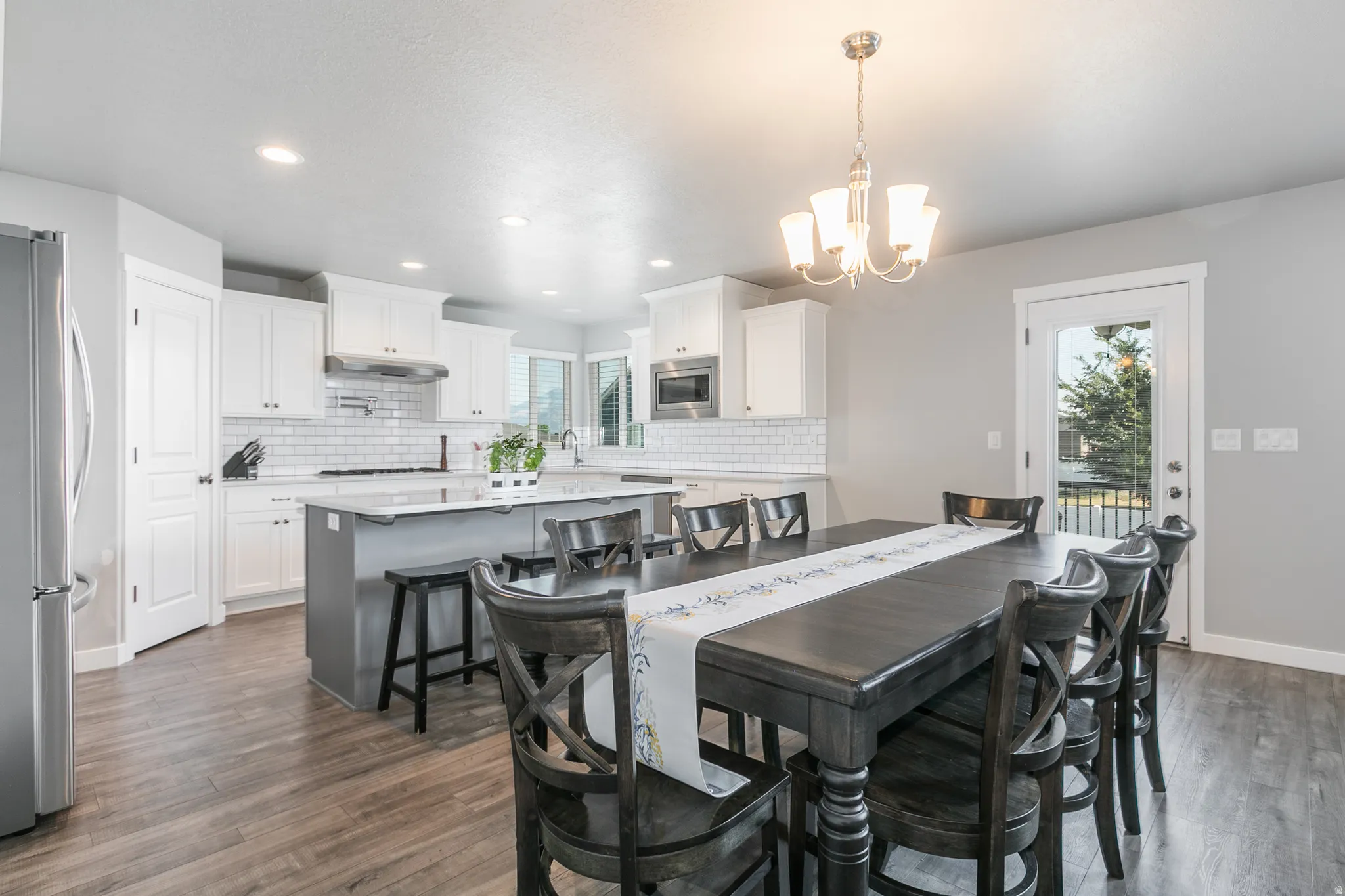 Open-concept kitchen and dining area featuring wood-finish flooring, white cabinetry, subway tile backsplash, and stainless steel appliances