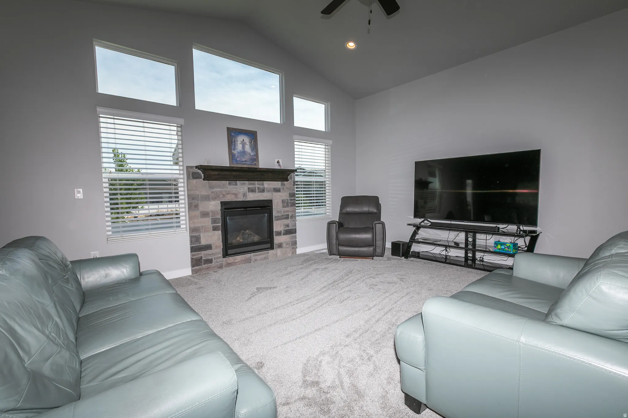 Living area featuring a stone-clad fireplace with a dark wood mantel, vaulted ceilings, and high windows