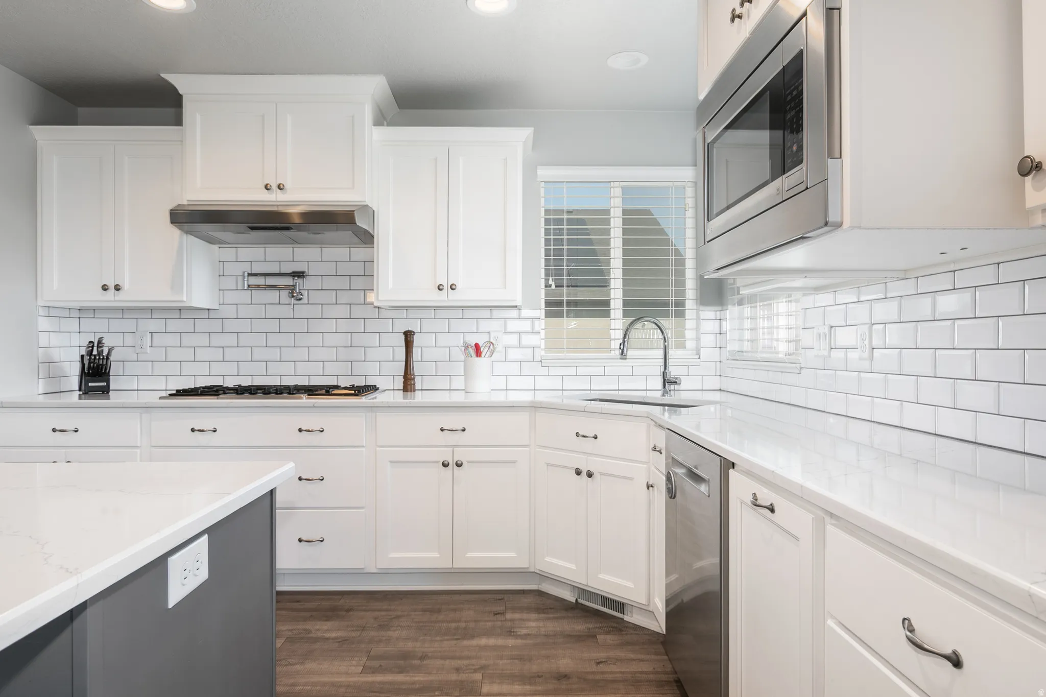 Modern kitchen featuring white cabinetry with dark hardware, a subway tile backsplash, stainless steel appliances, and wood-finish flooring