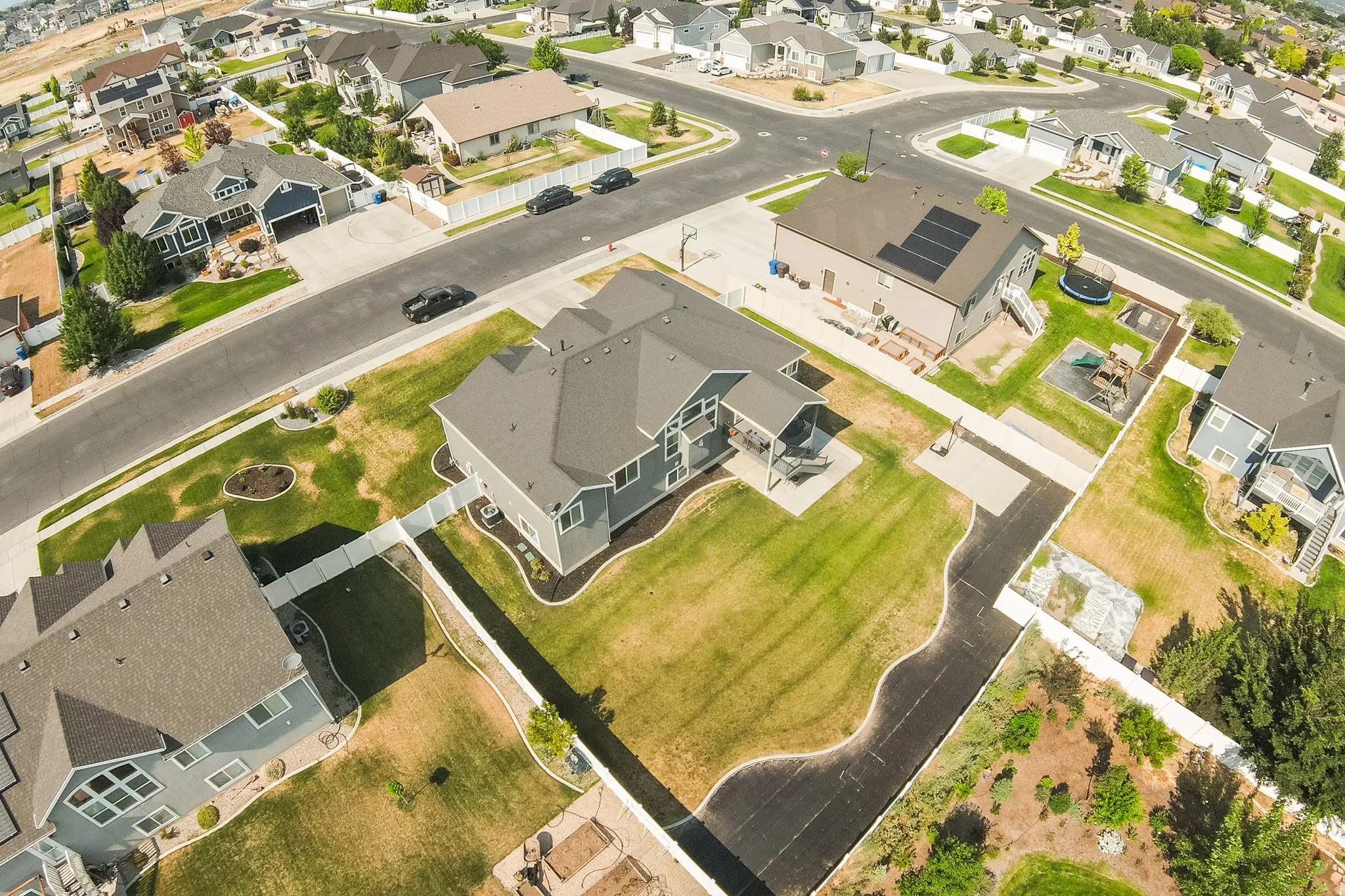 Spacious residential property featuring a large backyard with manicured lawn, an extended paved driveway, and a covered patio