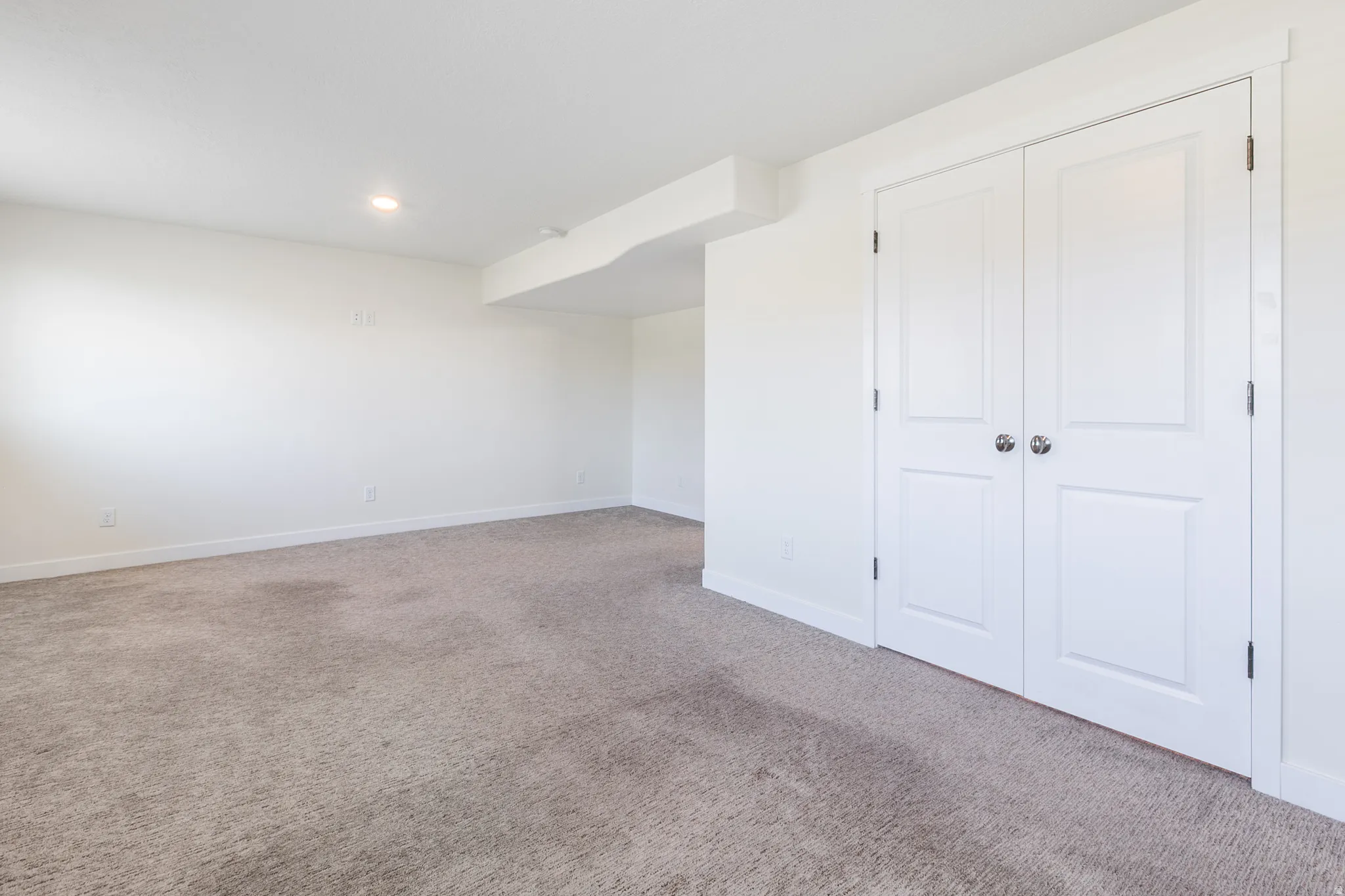 Spacious room featuring neutral carpeting, white walls, and a pair of double panel doors with brushed nickel hardware