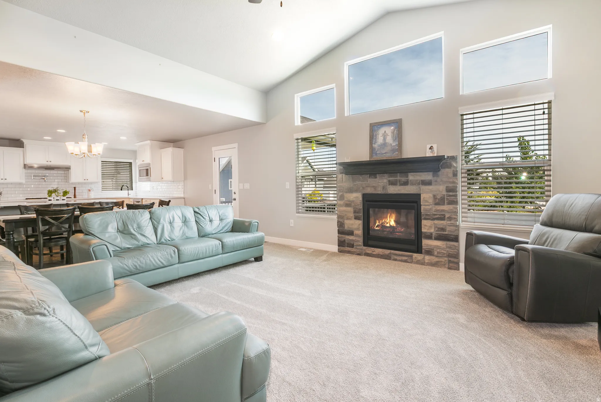 Living area featuring a stone-clad fireplace with a dark wood mantel, vaulted ceilings, and upper transom windows