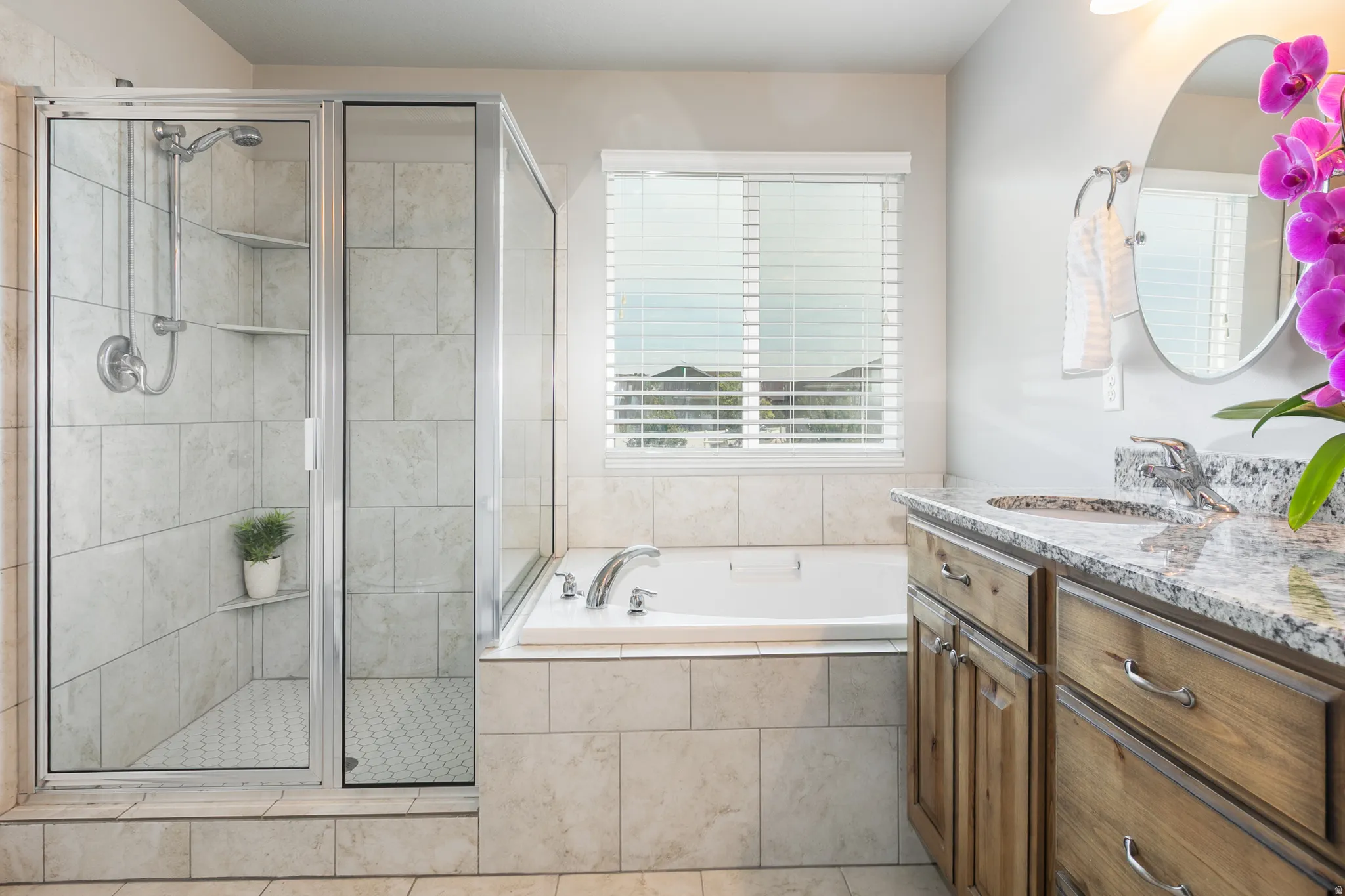 Bathroom featuring a walk-in shower with tile surround, a built-in soaking tub, a single vanity with a granite countertop, and a window with horizontal blinds
