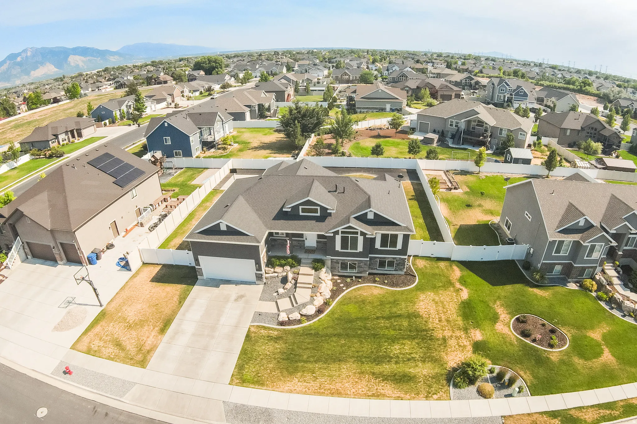 Modern residential exterior with dark siding and white trim, featuring a multi-car driveway, an attached garage, and a landscaped front yard with decorative rocks