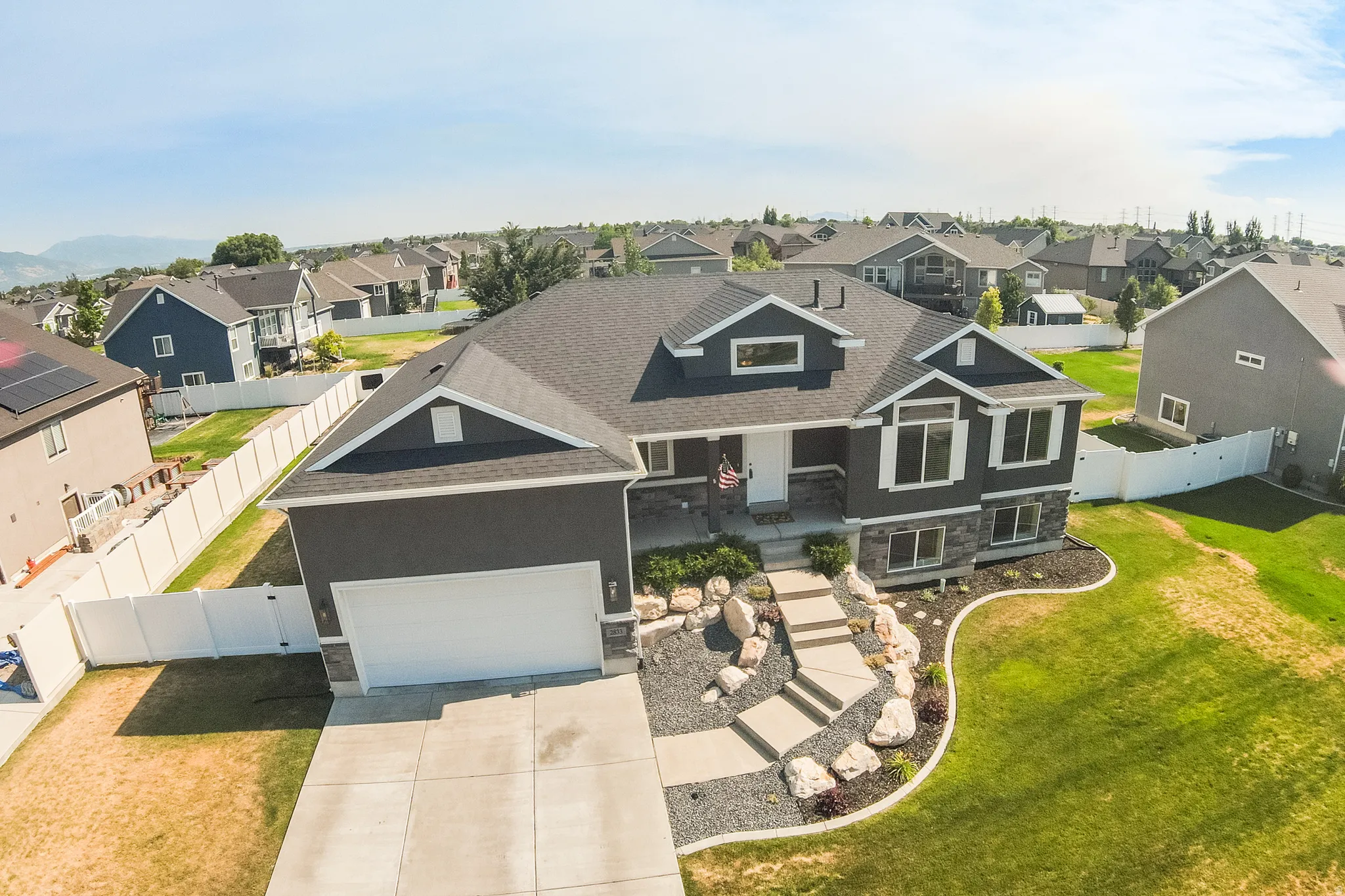 Split-level residence featuring a dark gray facade with white trim, a two-car garage, and a tiered stone and gravel pathway