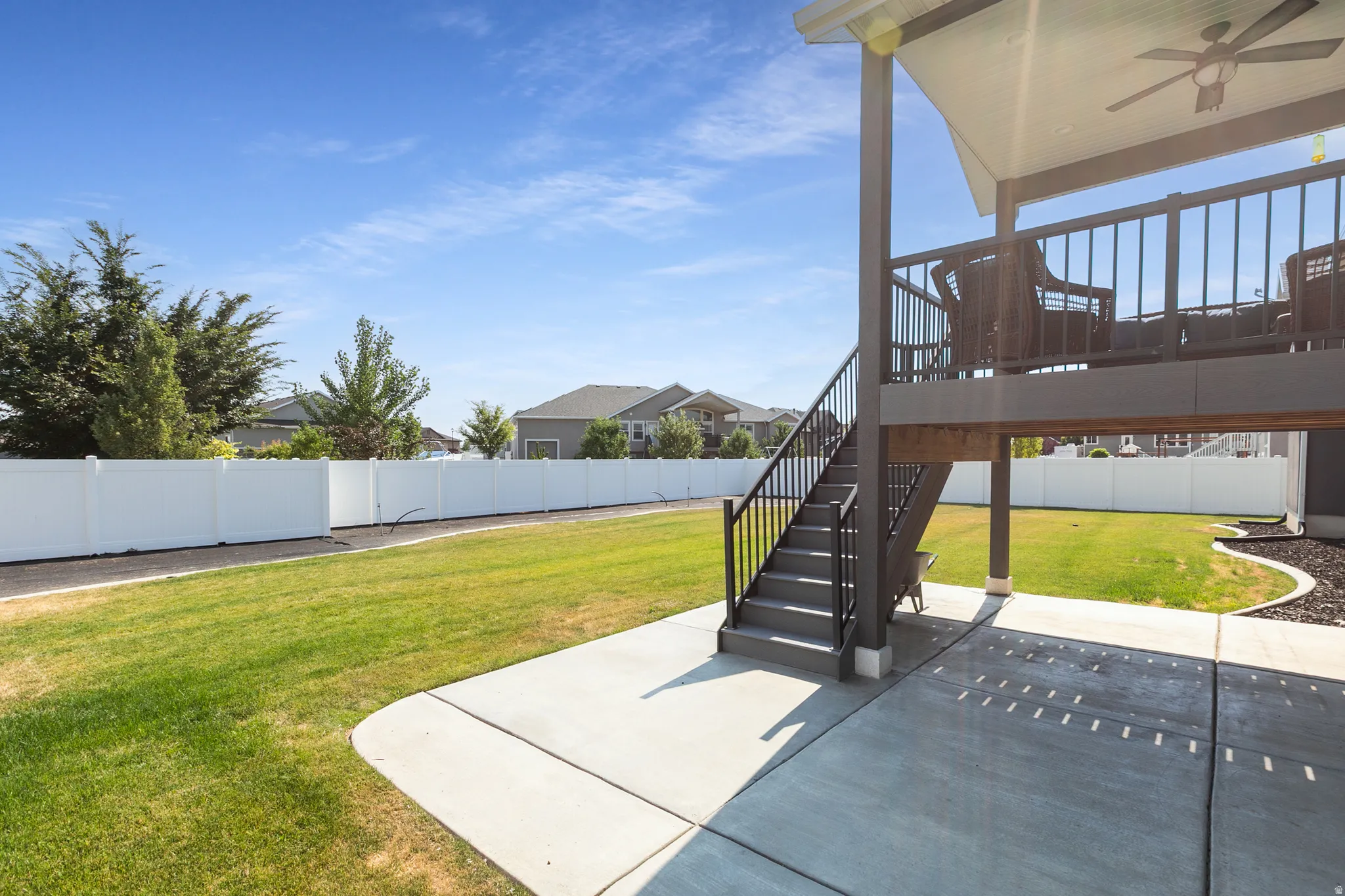 Expansive outdoor area featuring a spacious patio, a manicured lawn, and a white privacy fence