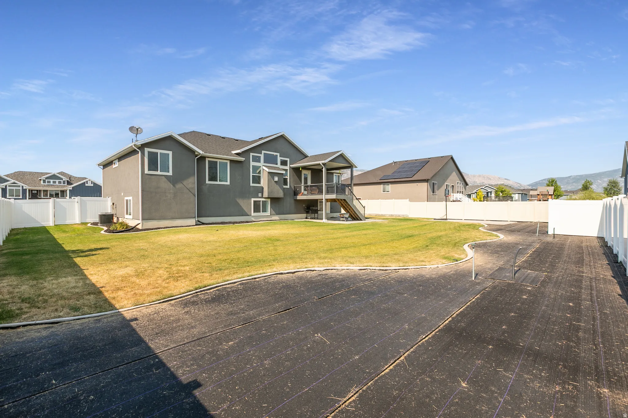 Spacious backyard featuring a manicured lawn, white vinyl fencing, and a covered upper deck