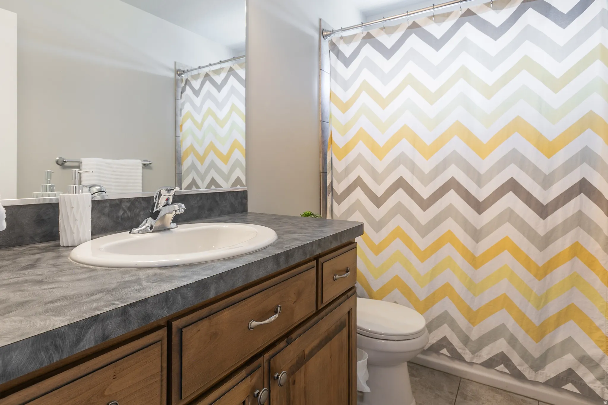 Bathroom vanity featuring a light wood-finish cabinet with silver hardware, a single basin sink, and a dark stone-look countertop