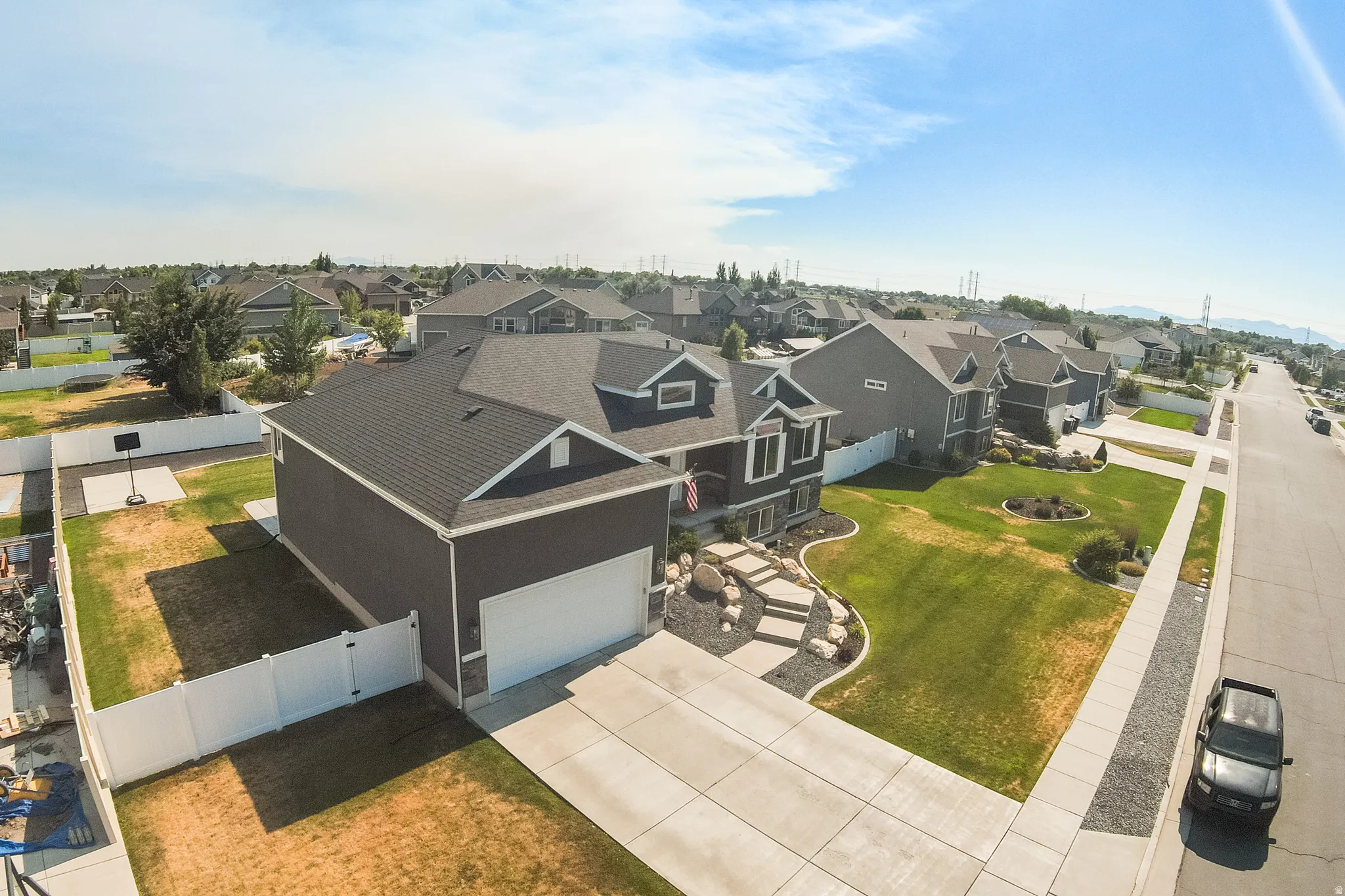 Charcoal gray two-story residence featuring a white garage door, concrete driveway, and front yard landscaping with natural stone elements