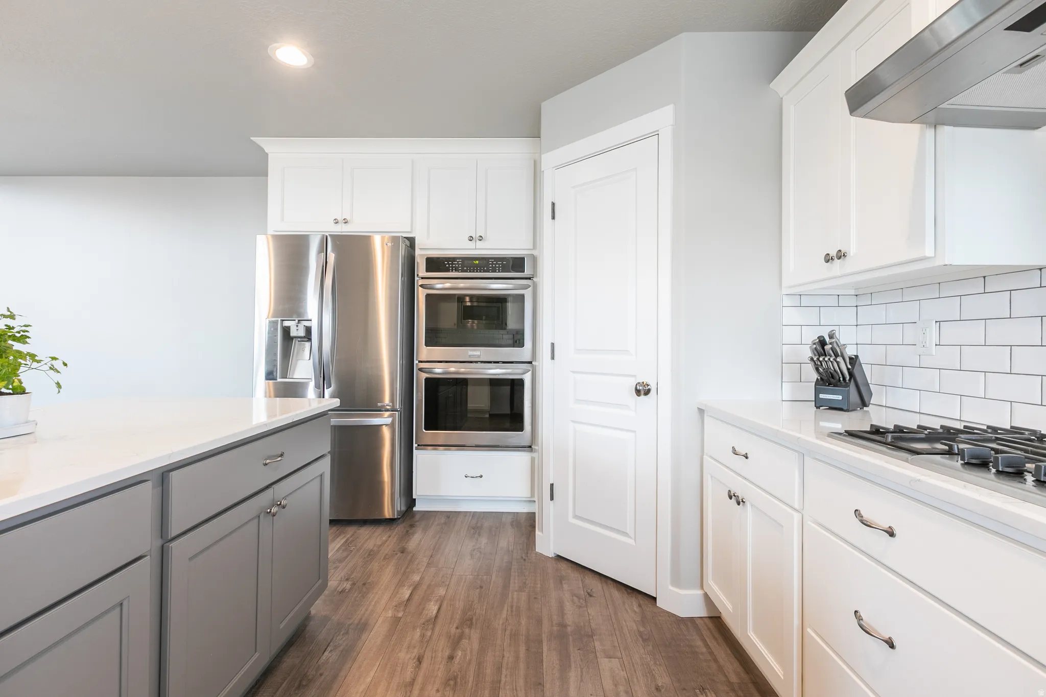 Modern kitchen featuring stainless steel appliances, white cabinetry, a built-in double oven, wood-finish flooring, and subway tile backsplash