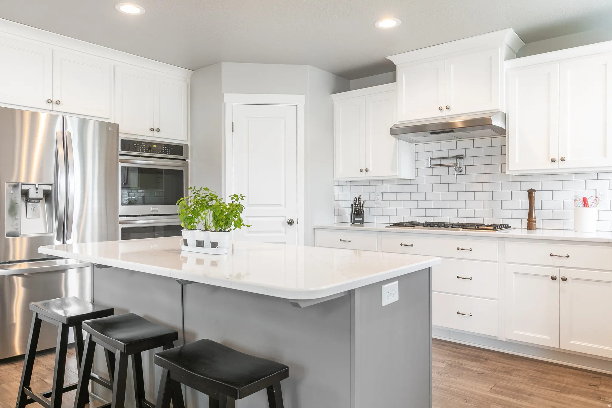 Contemporary kitchen featuring an oversized island with seating, white shaker cabinetry, white subway tile backsplash, stainless steel appliances, and wood-finish flooring