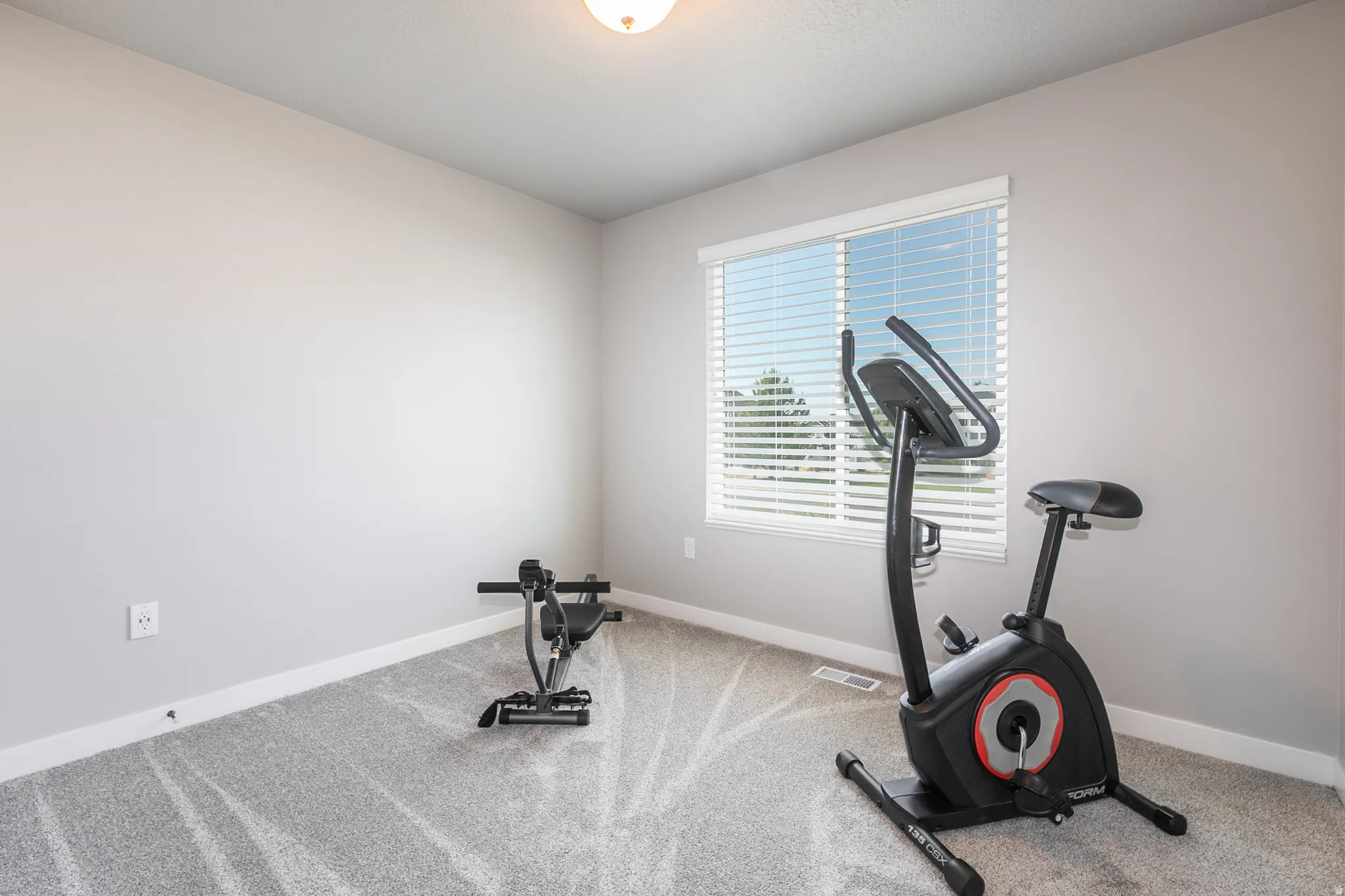 Carpeted room with light gray walls, a single window featuring horizontal blinds, and white baseboards