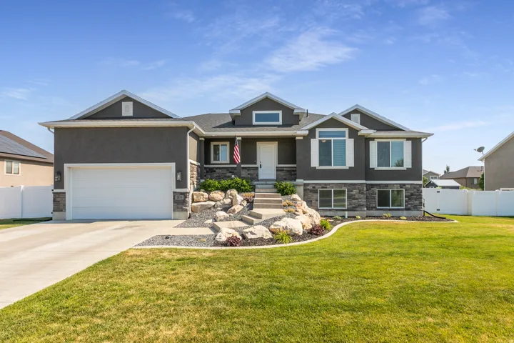 Modern gray stucco exterior with a stone veneer accent, featuring a two-car garage, white trim windows, and a landscaped front yard with decorative rocks
