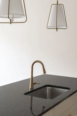 Integrated stainless steel sink, bronze-finish gooseneck faucet, dark granite countertop, and two contemporary pendant lights