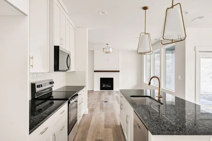 Modern kitchen featuring dark granite countertops, white cabinetry with gold-tone hardware, and wood-finish flooring