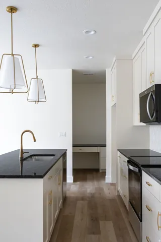 Kitchen featuring a peninsula with integrated sink and brass faucet, recessed lighting, wood-finish flooring, white cabinetry with brass hardware, and black countertops