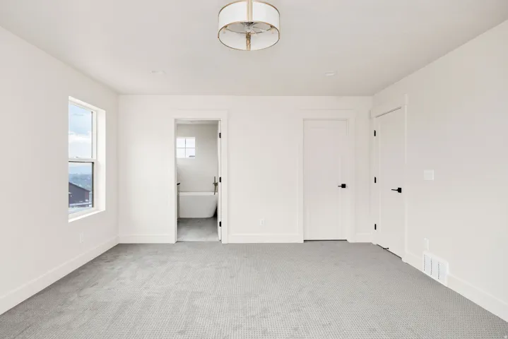 Bright room featuring neutral carpeting, a large window, and an en-suite bathroom with a freestanding tub