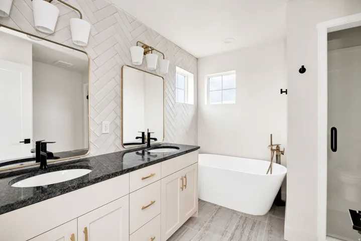 Double vanity with dark countertops, white cabinetry, and gold hardware