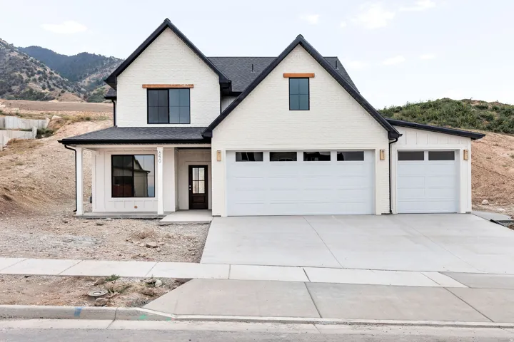 Contemporary white brick exterior with black framed windows, dark shingle roof, wood accent porch beam, and two white garage doors