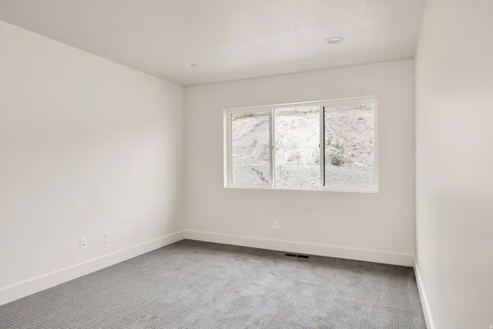 Recessed lighting illuminates this room featuring light gray carpeting, white walls, and a multi-pane window
