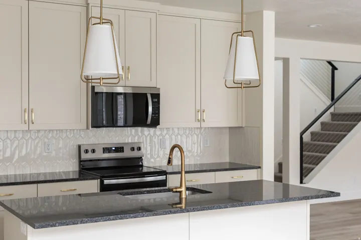 Kitchen featuring light-toned cabinetry, stainless steel appliances, dark countertops, and a decorative tile backsplash