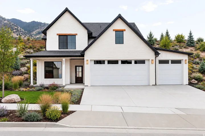 White brick exterior with black framed windows, a covered front porch, and an attached two-car garage