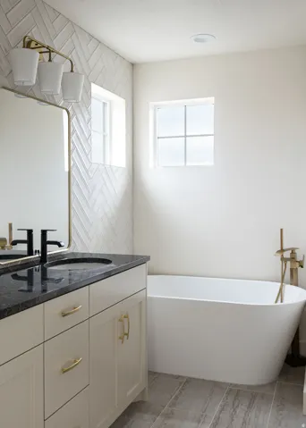 Vanity with a dark countertop and undermount sink, freestanding soaking tub, herringbone tile accent wall, and tiled flooring