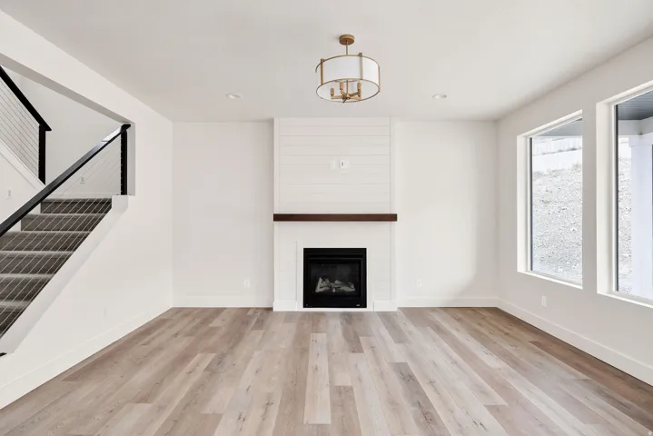 Wood-finish flooring, staircase with metal railings, built-in fireplace with shiplap accent, and a modern drum light fixture