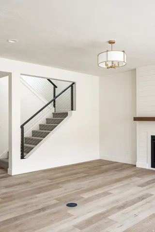 Wood-finish flooring, staircase with metal railing, drum chandelier, shiplap accent wall, and built-in fireplace