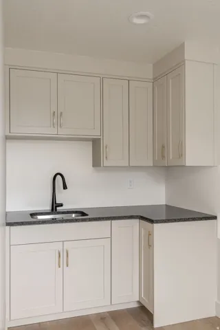 Corner wet bar with a stainless steel sink, black faucet, light grey cabinetry, and dark countertop