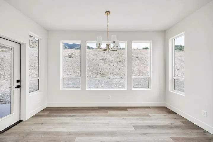 Spacious room featuring wood-finish flooring, a contemporary chandelier, multiple windows, and a glass-paneled door