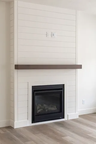 Contemporary fireplace featuring a black insert, a wood-finish mantel, and shiplap paneling