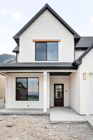 White brick and board-and-batten exterior with black-framed windows, a dark wood-finish entry door, and an exterior wall sconce