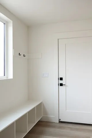 Built-in storage bench with open cubbies, wall-mounted coat rack, durable wood-finish flooring, and a modern interior door with matte black hardware