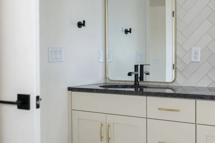 Vanity with integrated sink, dark countertop, and warm white cabinetry with gold-tone hardware