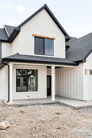 Modern farmhouse exterior showcasing crisp white brick siding with black trim, a steeply pitched gable roof with architectural detailing, and a recessed entry with a white garage door
