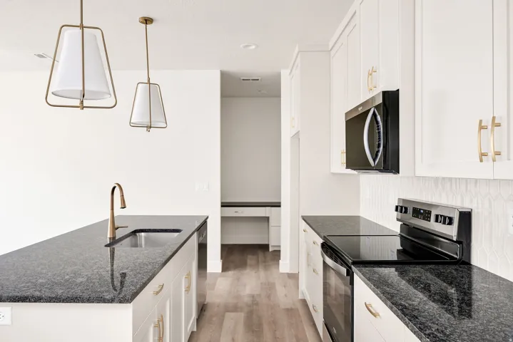 Kitchen featuring white cabinetry, dark stone countertops, stainless steel appliances, and two pendant light fixtures
