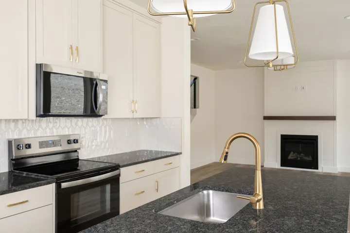 Kitchen featuring stainless steel appliances, dark stone countertops, white shaker-style cabinetry, and a gold-finish gooseneck faucet with an undermount sink