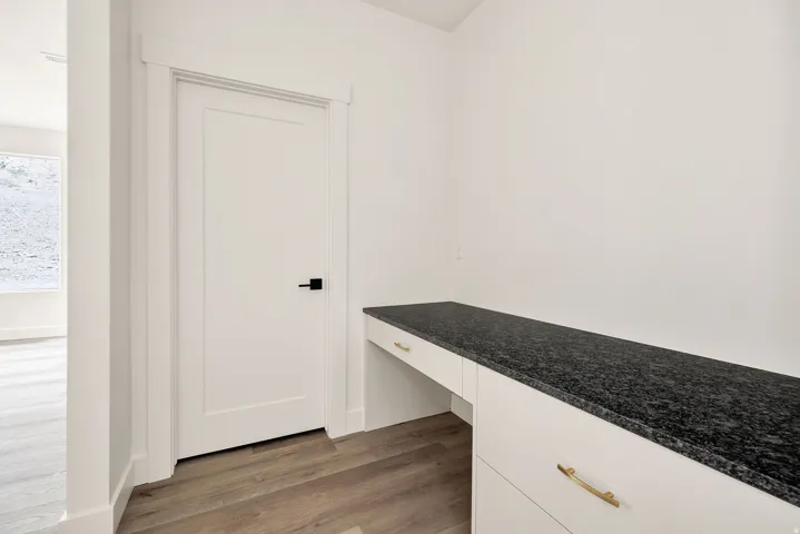 Built-in desk with a dark countertop, gold-toned drawer pulls, and wood-finish flooring