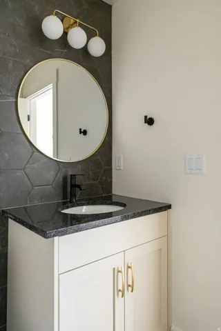 Vanity with white cabinetry and gold-finish hardware, built-in sink, dark countertop, and matte black faucet
