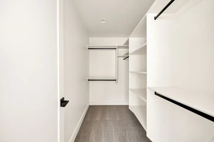 Walk-in closet featuring white built-in shelving, black hanging rods, and recessed lighting