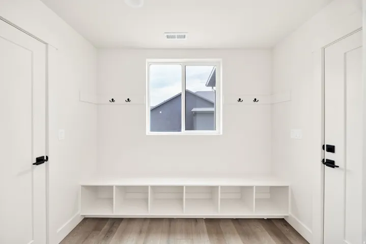 Built-in bench with cubby storage, wall-mounted coat hooks, wood-finish flooring, and a window for natural light