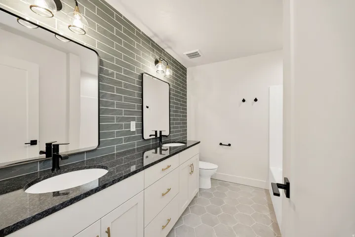 Dual vanity with black countertops, white cabinetry, and gold-tone hardware